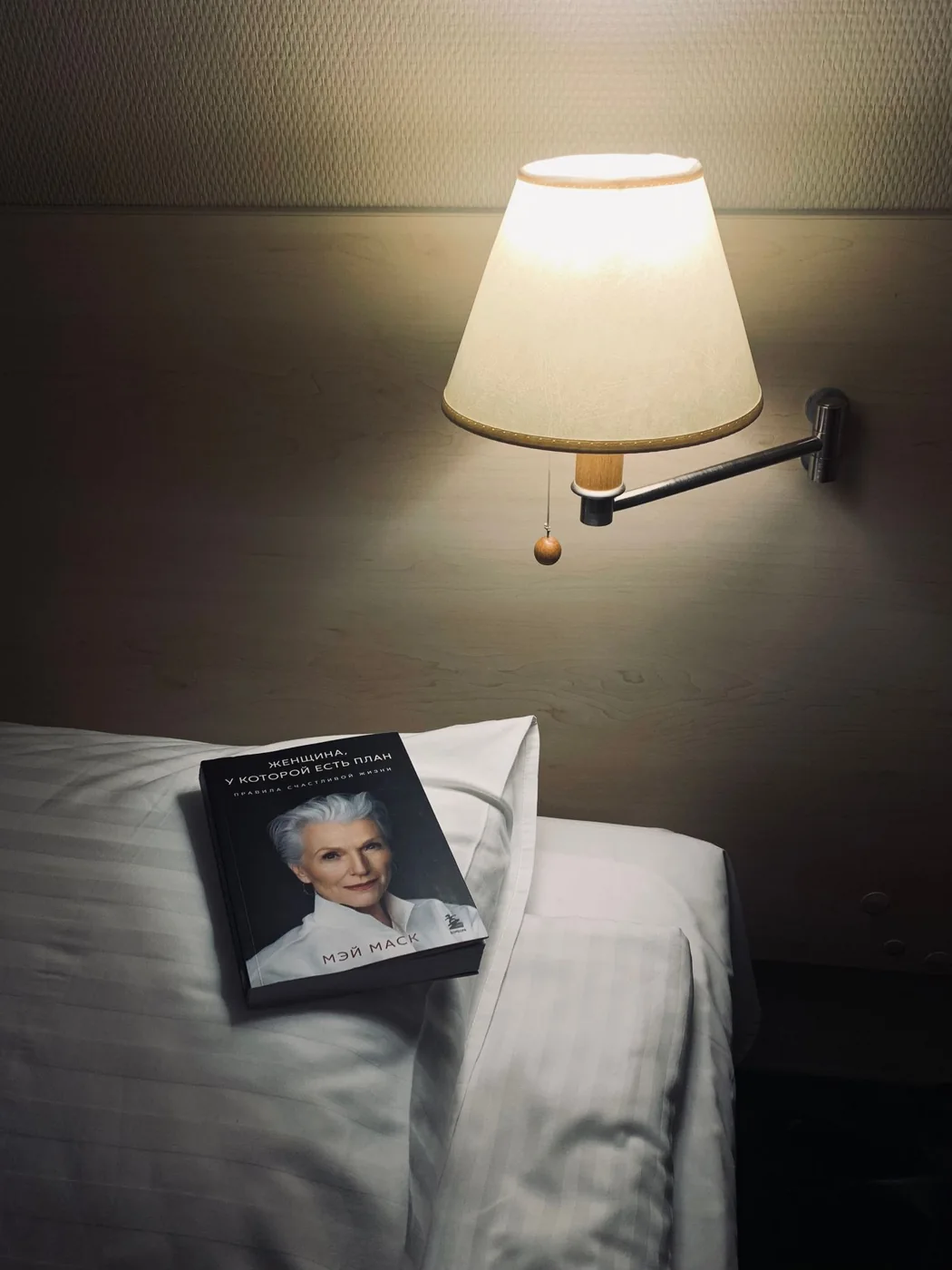 Book on a bed beneath a warm bedside lamp