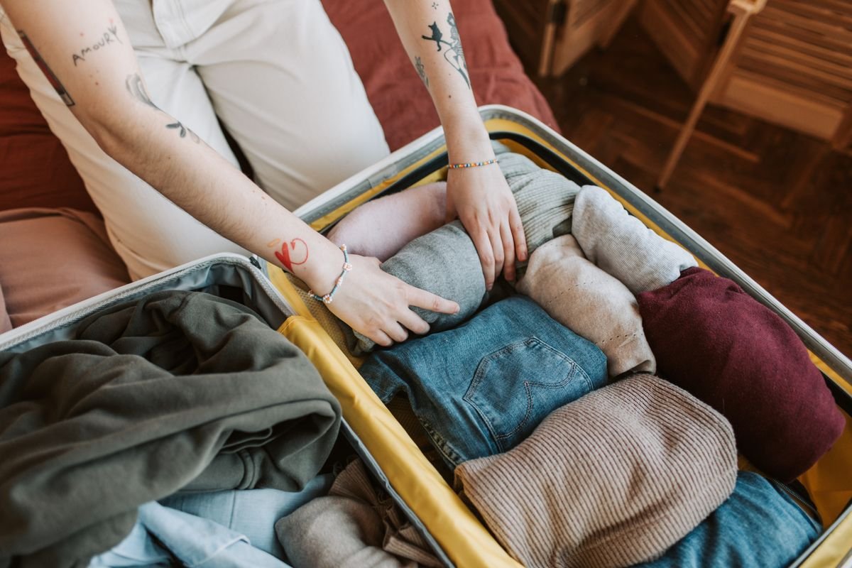 Hands packing clothing into an open suitcase before a trip