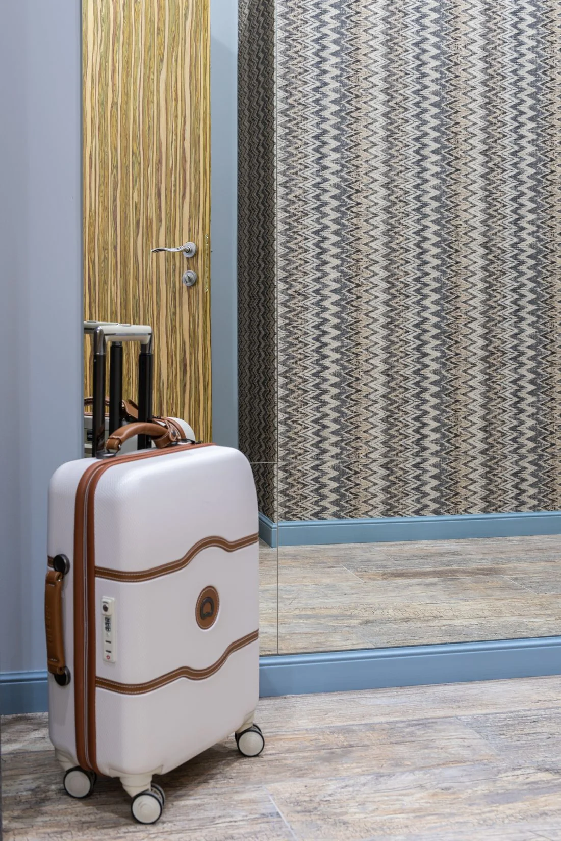 Pale suitcase beside a mirrored wall and closed door