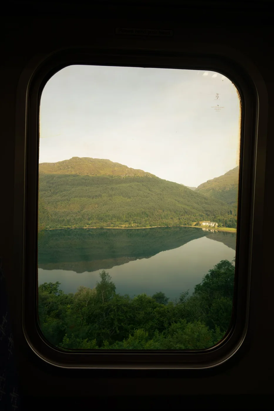 A lake and green hills seen through a train window