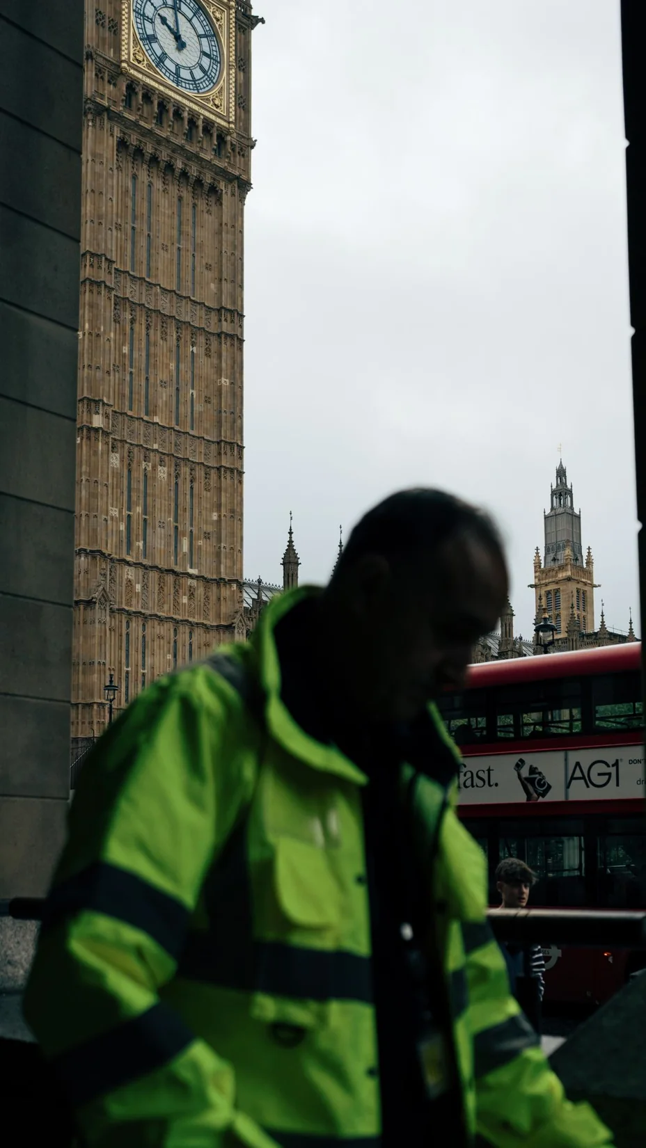 A red bus and a foreground pedestrian beside stone buildings on a London street