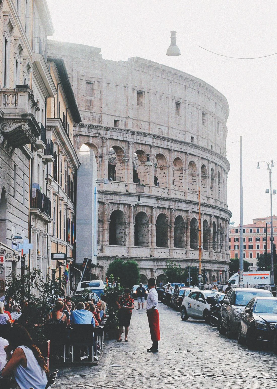 The Colosseum above a busy Rome street with people and vehicles