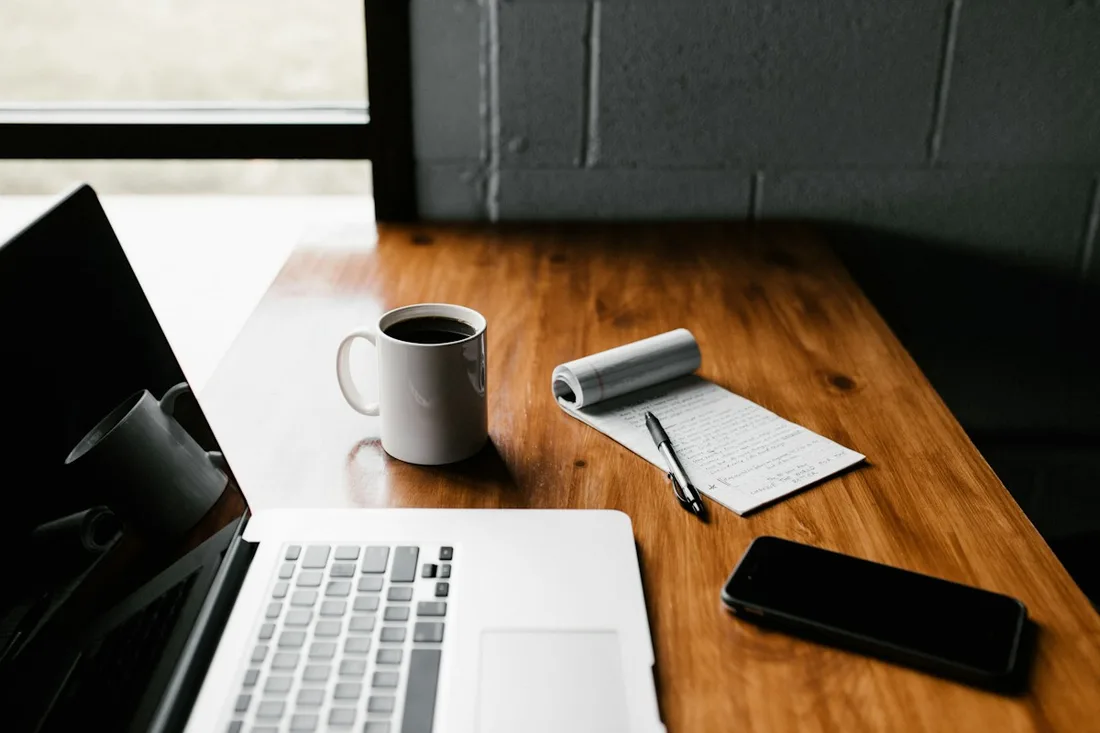 Laptop, mug, notebook and phone arranged on a wooden table