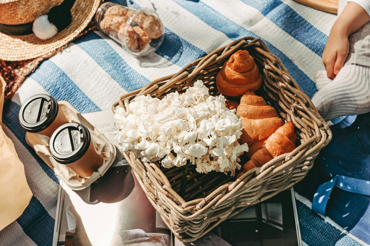 A picnic with croissants, donuts, and coffee on a blue and white striped blanket