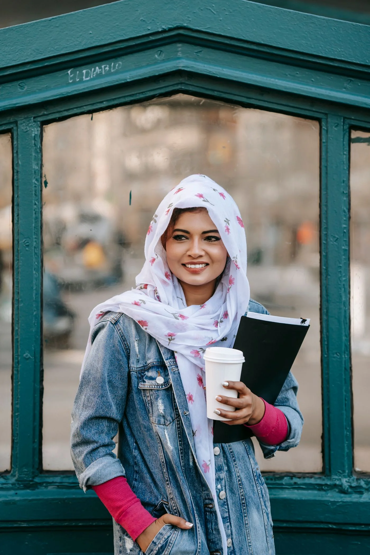 A woman holding a document folder and takeaway cup outdoors.